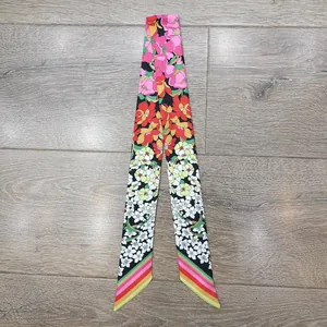 Dettaglio di sciarpa in seta floreale con peonie rosa e strisce arcobaleno su fondo legno