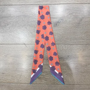 Detalle de pañuelo de seda naranja con estampados de hojas sobre fondo de madera