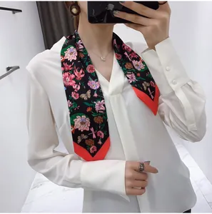 Detail of floral silk scarf with butterfly print and contrasting red edges on a blouse