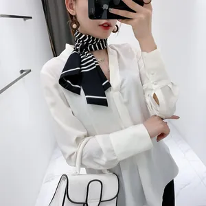 Macro view of white satin V-neck shirt paired with a chic black and white striped scarf
