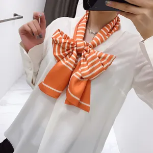 Detail of a bright orange and white striped skinny scarf tied in a large bow on a white shirt