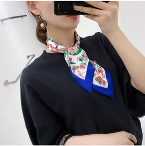 Detailed view of a narrow floral silk twilly scarf with blue ends worn around the neck