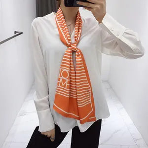 Detail of orange and white striped skinny silk scarf with HOM lettering on a model
