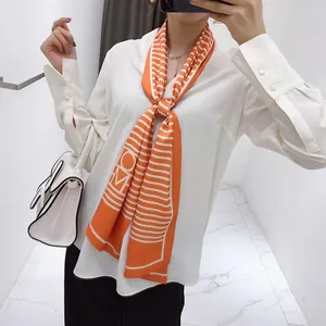 Detail of a long orange striped silk scarf with H letter logo tied on a white shirt
