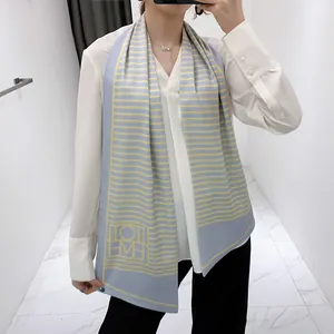 Detail view of a long blue silk scarf featuring yellow horizontal stripes and geometric logo