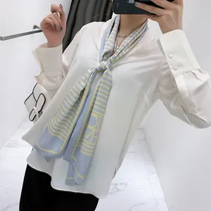 Close-up of a striped silk scarf with H-pattern styled on a white chiffon shirt collar