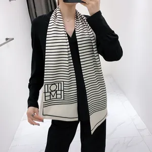 Detail of elegant slim silk scarf with black stripes and geometric logo on cream fabric