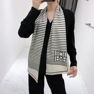 Detail of thin long scarf with black stripes and geometric logo on cream fabric