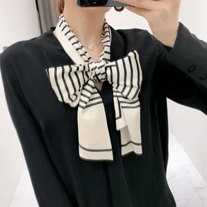 Elegant black and white striped narrow silk scarf tied in a bow on a black V-neck shirt