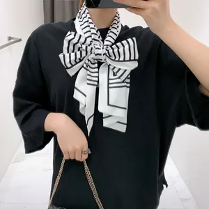 Detail of black and white striped silk scarf tied in a large bow knot over black t-shirt