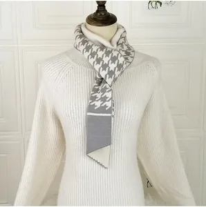 Detail of grey houndstooth knit scarf with button accent on a white turtleneck
