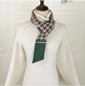 Detail of green and pink houndstooth knit scarf styled on a white turtleneck sweater