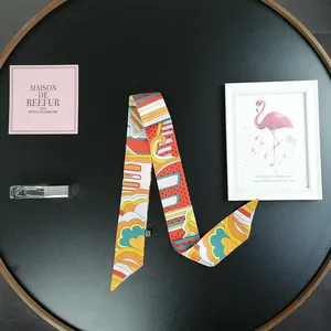 Dettaglio ravvicinato di un foulard twilly in seta con motivi geometrici colorati su vassoio