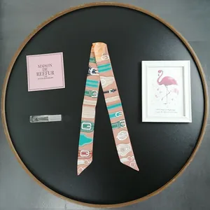 Detailed close-up of a long twilly silk scarf with vintage belt buckle pattern in pink and green