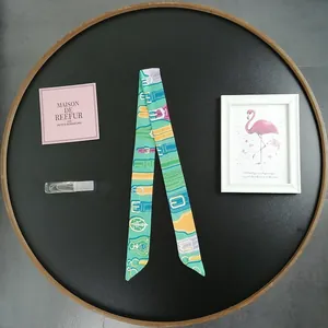 Close-up of a long skinny silk scarf with vibrant belt buckle prints in a gift tray