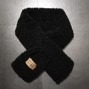 Close-up of black faux lamb wool scarf with stitched square brand label on grey texture