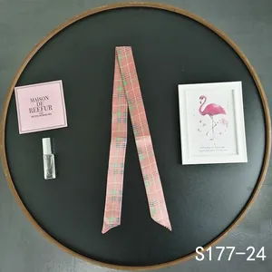 Detailed macro view of pink plaid skinny silk scarf wrapped on a round black tray