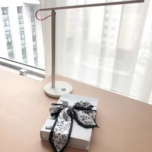 Foulard en soie blanche avec motif de feuilles noires noué en boucle sur un livre
