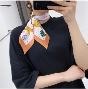 Detail of pink silk scarf with leopard and tropical leaf print knotted around neck
