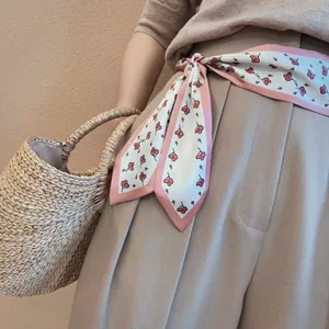 Close-up of a long skinny scarf with cherry print worn as a belt on khaki trousers