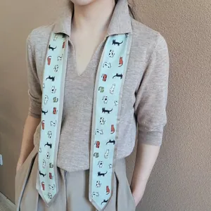 Detail van lichtblauwe zijden sjaal met cartoon kattenprints op een beige gebreide trui
