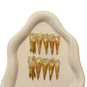 Artistic gold foil stiletto press-on nails with metallic liquid drip design on a ceramic tray