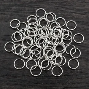Pile of silver metal jump rings for jewelry making on dark wood grain background