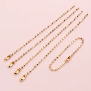Dettaglio di cinque catenelle a sfere dorate da 2mm in ferro con connettori su fondo rosa