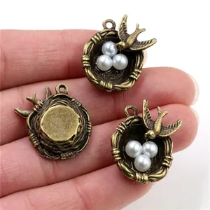 Three bronze bird nest pendants with white pearls and birds on a plain background
