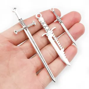Drei antike silberne Schwertanhänger für DIY-Schmuck auf einer Handfläche als Maßstab