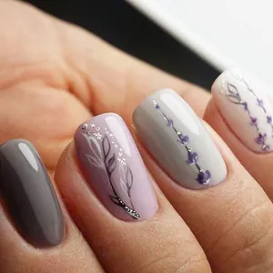 Primer plano de uñas postizas ovales con flores púrpuras y detalles de brillo plateado