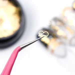 Gold hollow heart-shaped nail charm with Love text held by pink tweezers for DIY art