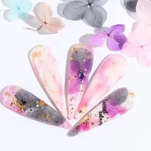 Close-up of stiletto press-on nails with purple dried flowers, gold foil, and rhinestones
