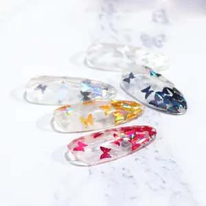 Detalle macro de lentejuelas de mariposa holográficas en uñas stiletto transparentes