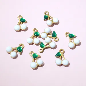 Close-up of gold cherry charms with green enamel leaves and white beads for DIY jewelry