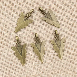 Fünf Vintage-Bronze-Pfeilanhänger für DIY-Schmuckherstellung auf beige-strukturiertem Grund
