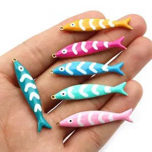 Detailed view of colorful enamel fish charms for DIY jewelry making held in a palm