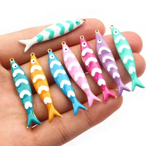 Handheld view of colorful fish enamel pendants for DIY jewelry making in eight vibrant colors
