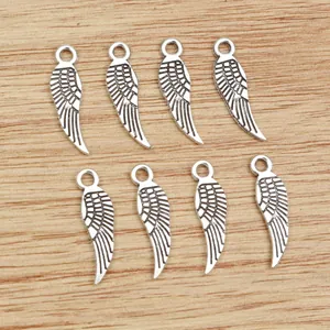 Eight vintage silver feather wing charms for DIY jewelry making on wood background