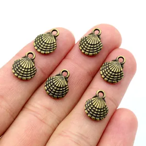 Macro detail of six shell-shaped alloy charms for jewelry making held by a hand