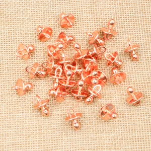 Macro shot of rose gold pacifier charms for DIY jewelry making on beige fabric