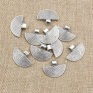 Macro detail of fan-shaped vintage silver charms with textured concentric arcs and loop