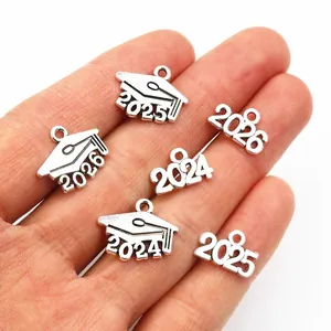Close-up of antique silver 2025 and 2026 graduation cap charms held in hand for size