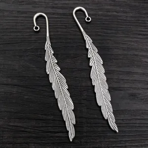 Pair of antique silver alloy feather charms with hooks for DIY necklaces on wood