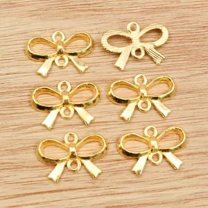 Detail of six gold alloy bow pendants for DIY jewelry making on a light wooden background