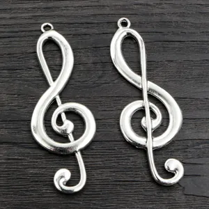 Pair of silver treble clef music note alloy pendants for DIY jewelry on wood background