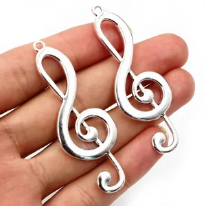 Silver musical G-clef treble note pendants held by hand to show 61x22mm size