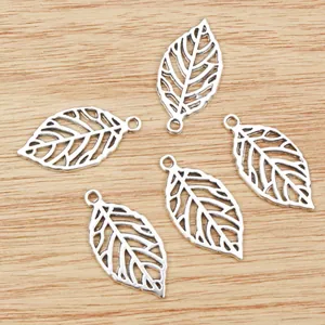 Five silver hollow leaf pendants for DIY jewelry making on a light wooden background