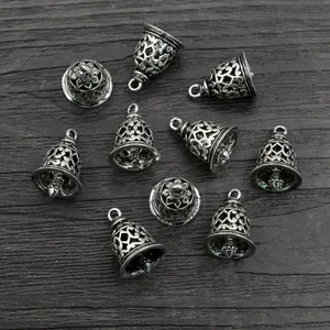 Group of 9 vintage silver brass bell charms with hollow floral patterns on dark wood background