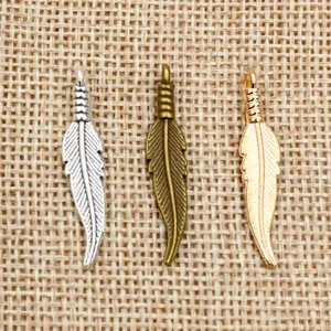 Détail de pendentifs plumes en alliage argent, bronze et or sur toile de jute